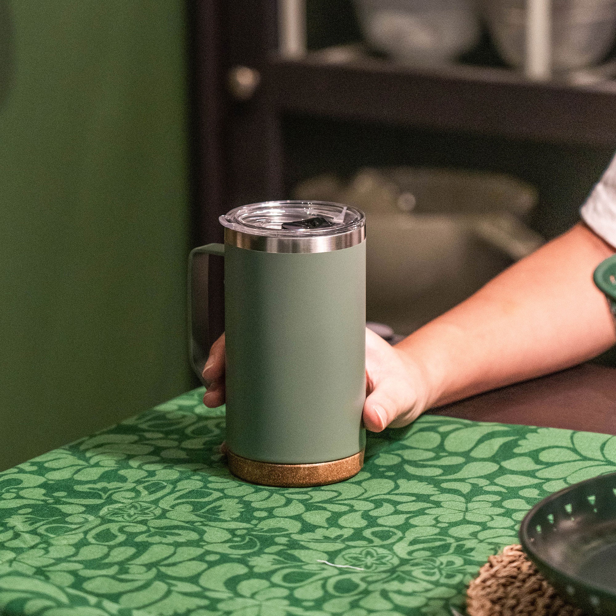 Hand placing the green 24 oz TYESO CASK insulated coffee mug on a dining table #color_green